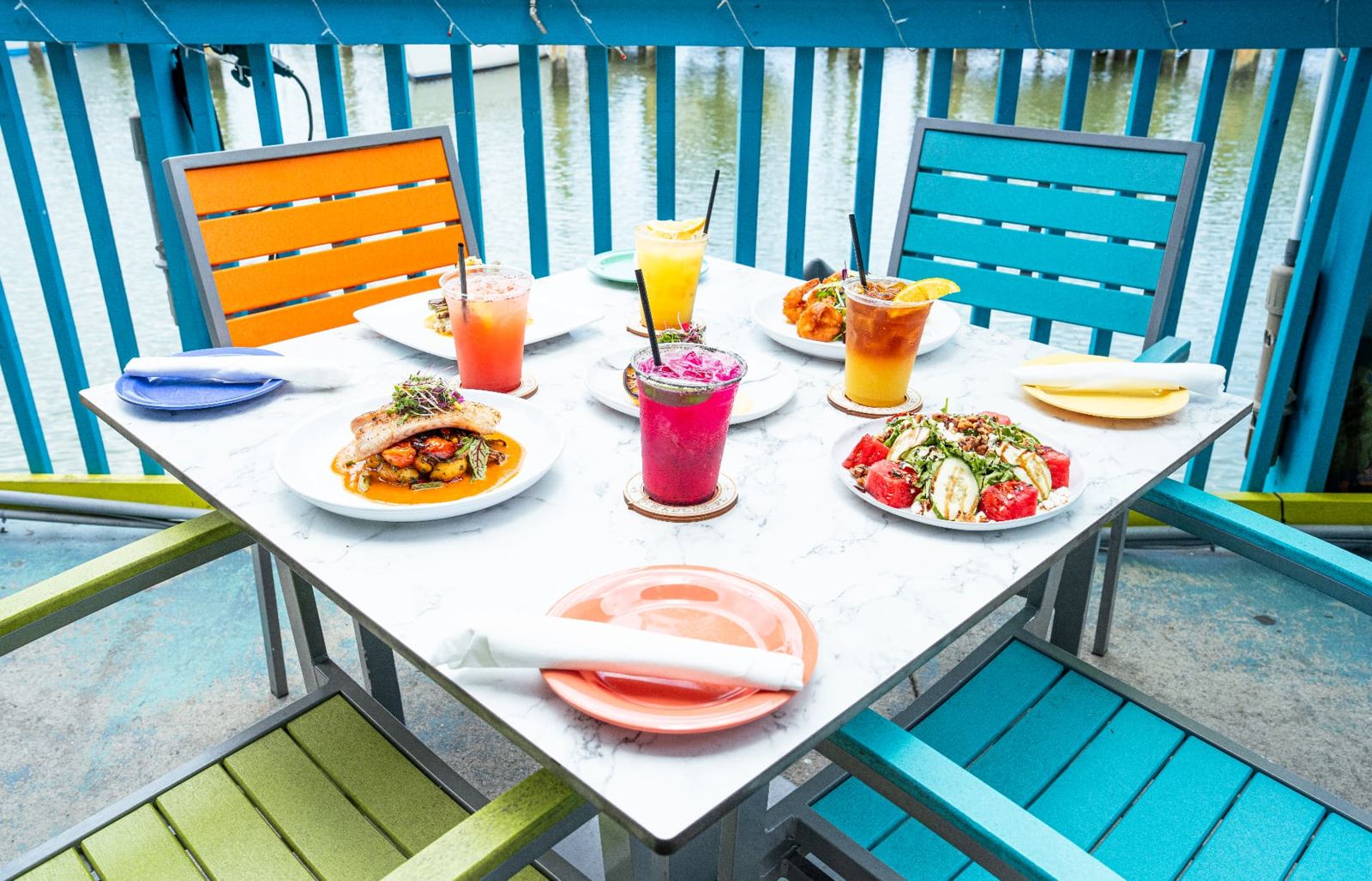 Colorful waterfront table loaded with cocktails and seafood dishes